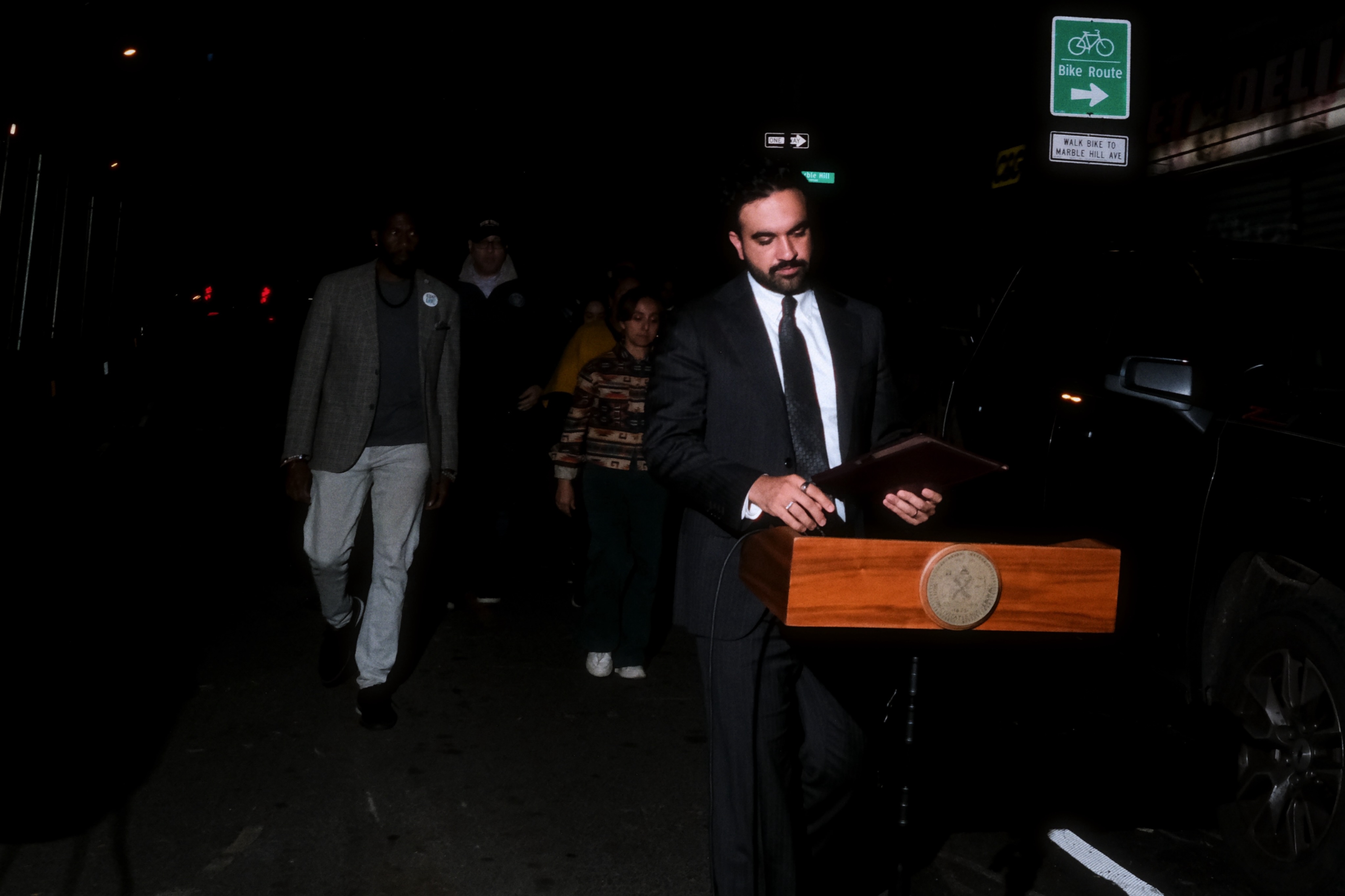 Zohran Mamdani speaking at an outdoor lectern at night.